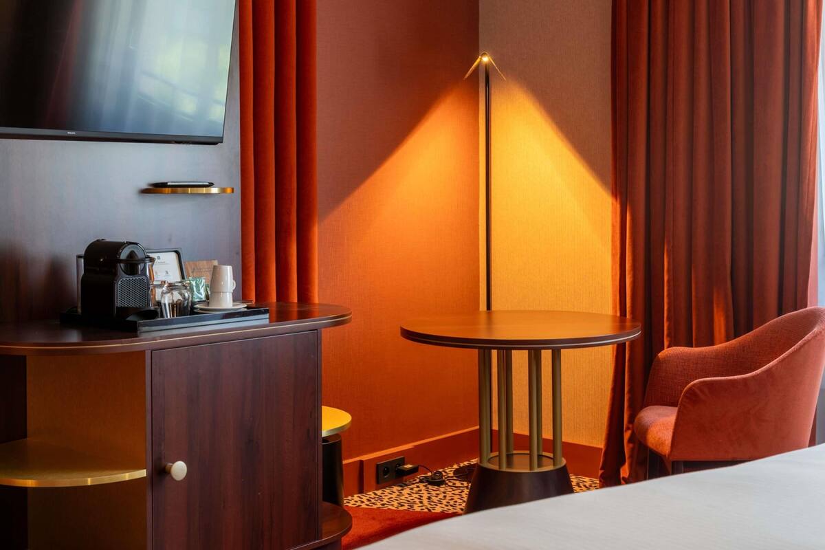 A hotel room with a bed, a TV, a desk with a coffee maker, a lamp, and a chair.