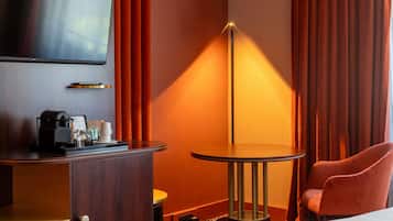 A hotel room with a bed, a TV, a desk with a coffee maker, a lamp, and a chair.