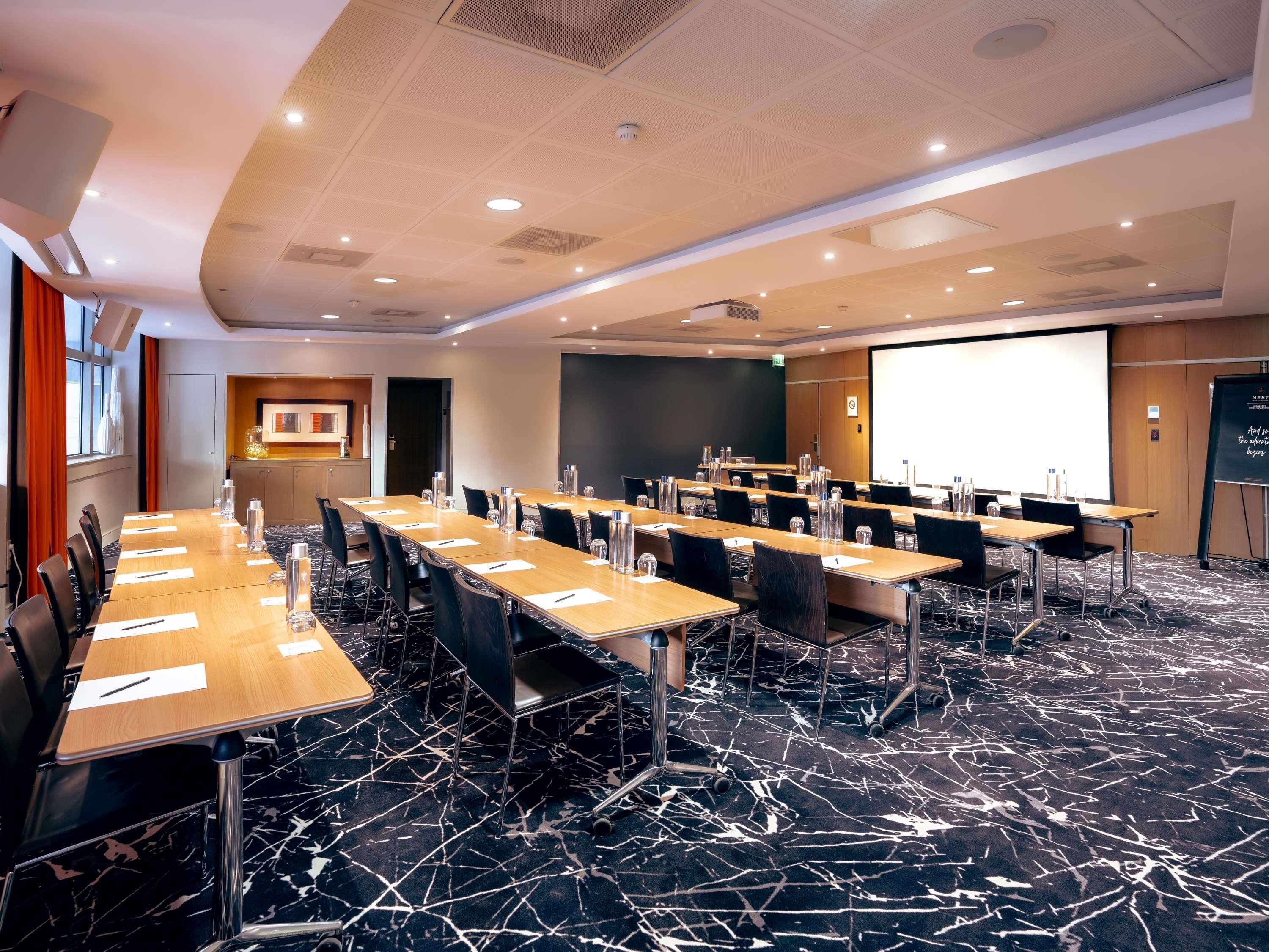 A conference room with a long table, chairs, a projector screen, and a presentation board.