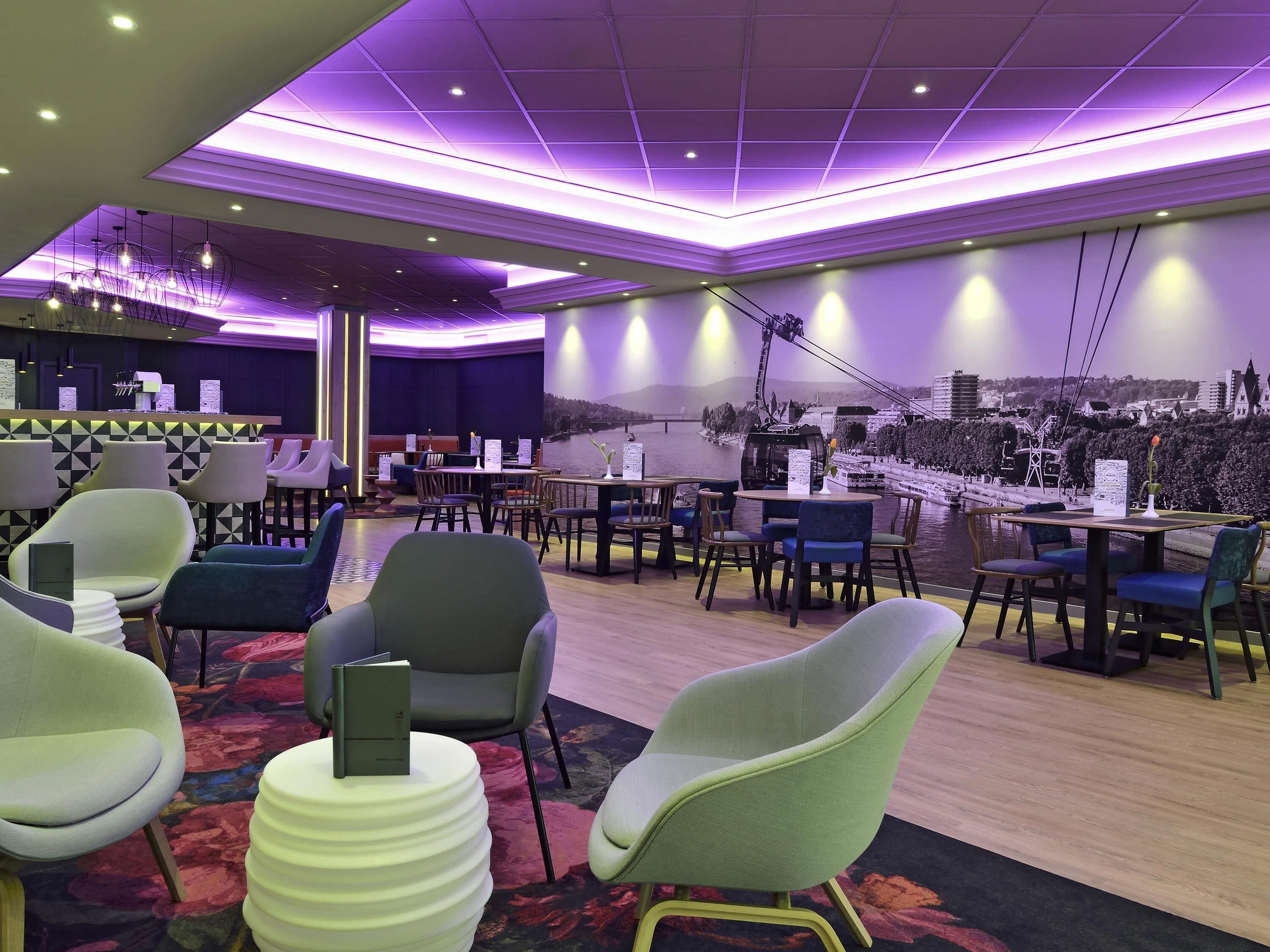 Un hall d’hôtel moderne avec un bar, des espaces aménagés pour s’asseoir et une vue sur le paysage urbain.