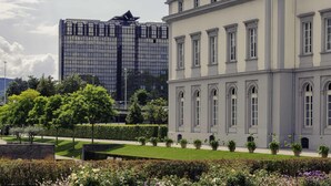 Un edificio clásico con ventanas simétricas y un edificio moderno de vidrio al fondo.