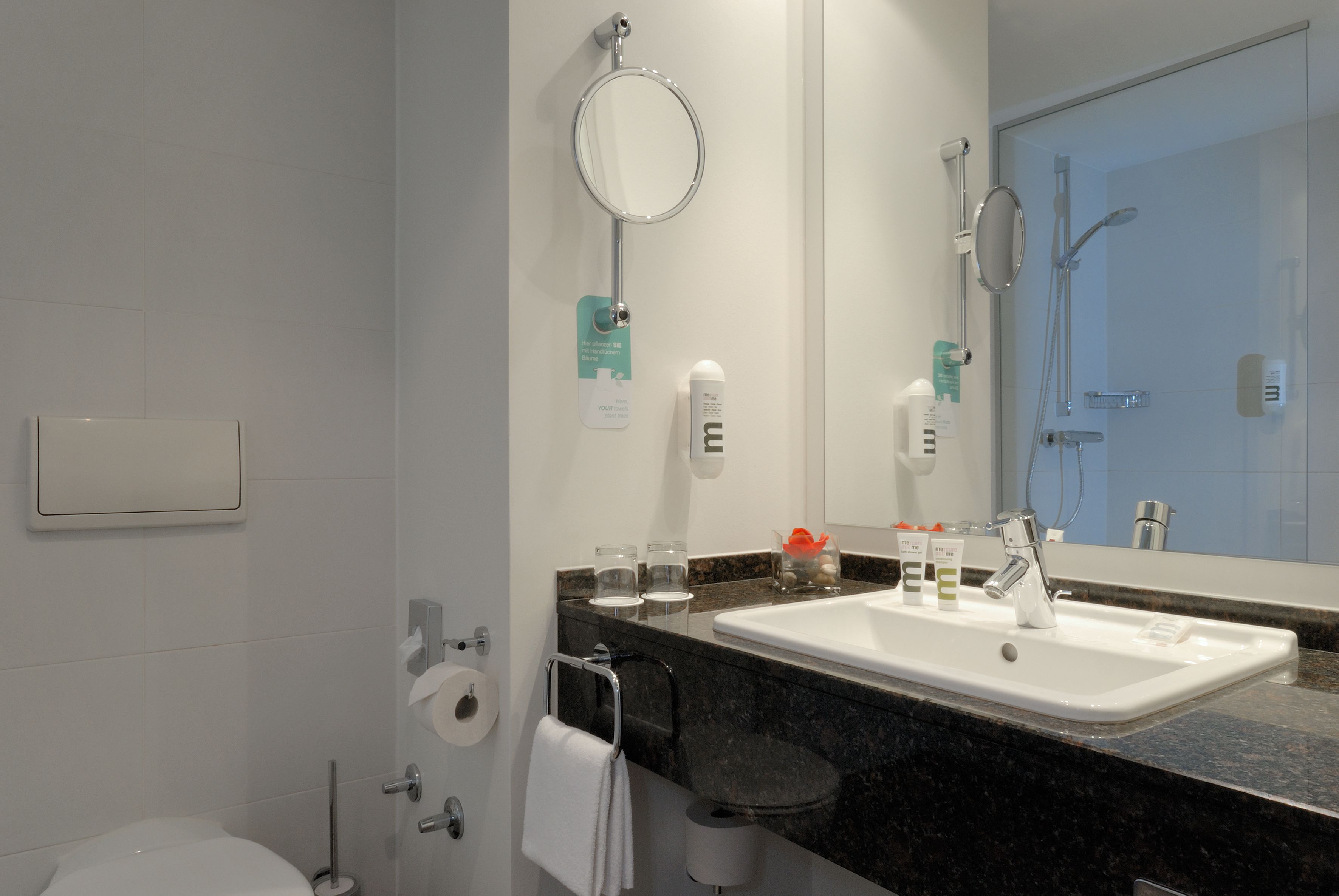 Un baño moderno con lavamanos blanco, un espejo grande, cerramiento de ducha de vidrio y un inodoro.