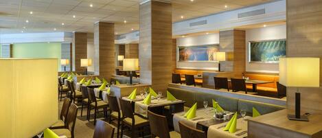 A modern restaurant with multiple dining areas, including booths and tables, and a bar area.