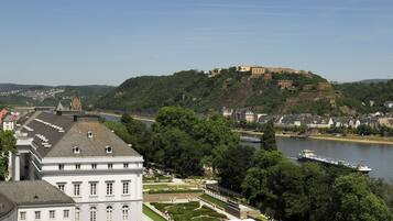 A historic building with a prominent tower, a river, and a castle on a hill in the background.