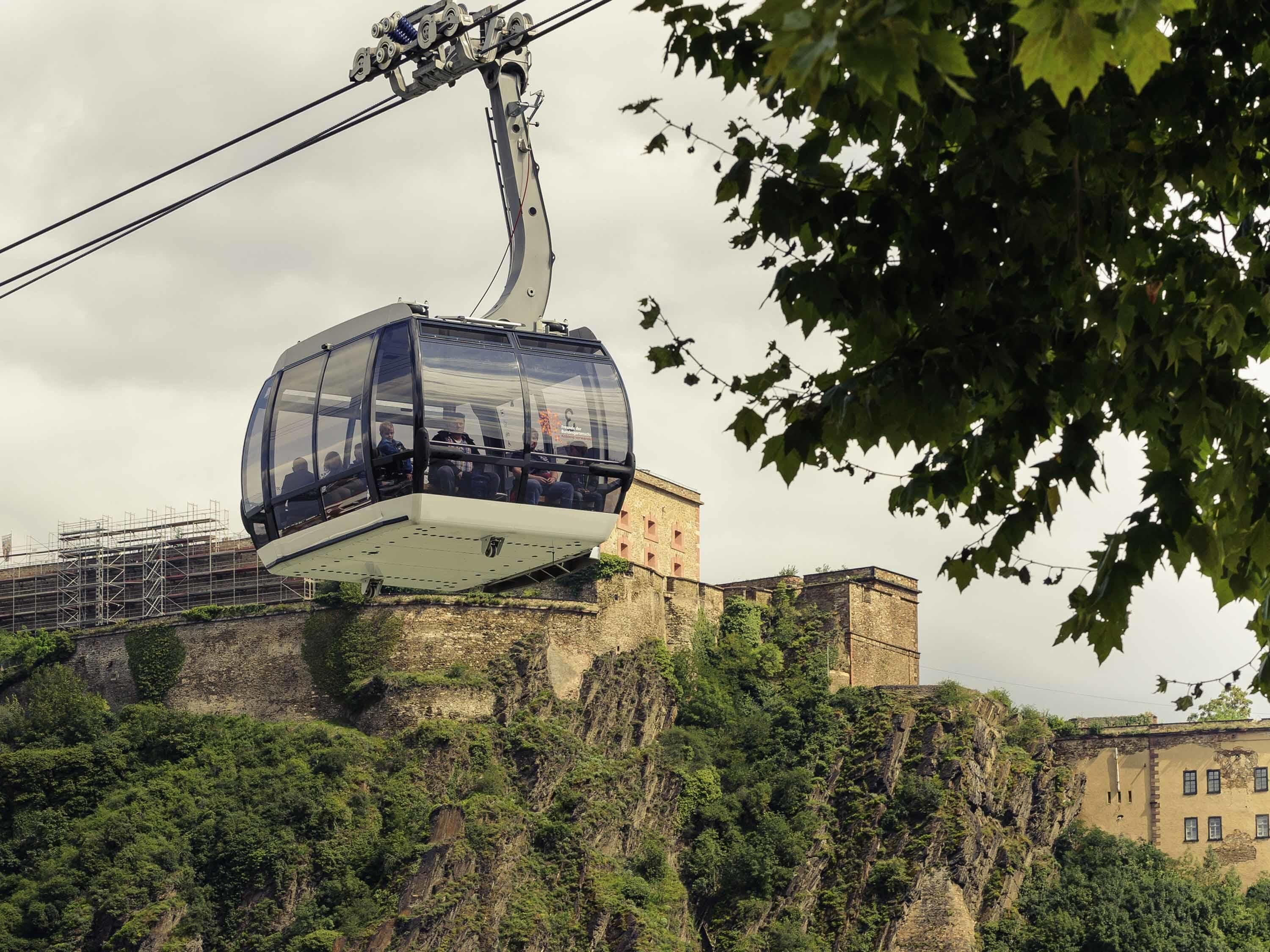 A cable car with passengers, a historic building, and surrounding greenery.