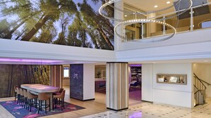 Un vestíbulo de hotel espacioso y moderno con techo alto, un área de bar central y vistas a árboles altos a través del vidrio.