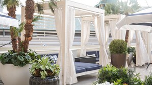 A covered outdoor seating area with a canopy, potted plants, and a view of a building with a dome. - The Windsor Court (New Orleans)