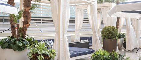 A covered outdoor seating area with a canopy, potted plants, and a view of a building with a dome.
