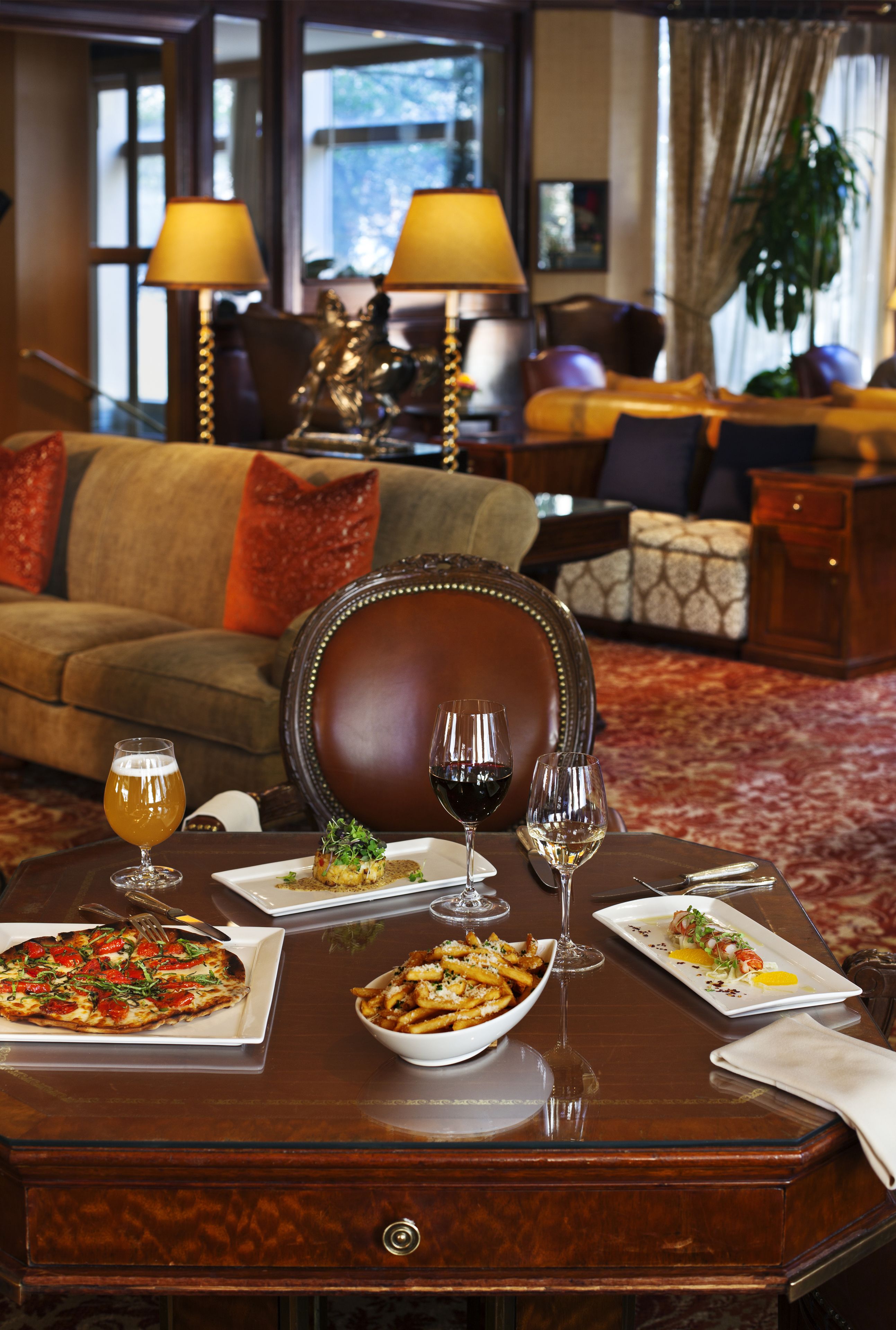 Una mesa de comedor dispuesta con diferentes platos, copas de vino y cubiertos en una habitación bien amoblada, con un sofá y lámparas al fondo.