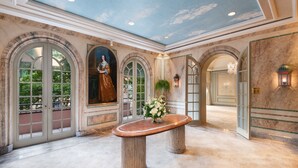 A lobby with marble flooring, arched doorways, a central table with a vase of flowers, and a ceiling mural. - The Windsor Court (New Orleans)