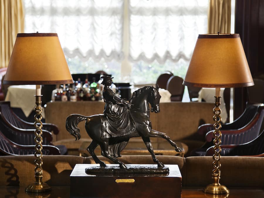 A room with a sofa, two lamps, a chandelier, and a statue of a horse.