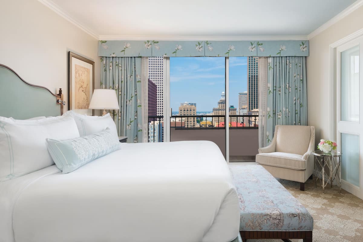 Quarto de hotel com uma cama grande, uma cadeira e vista para a paisagem urbana pela janela.