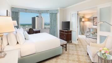 Quarto de hotel com uma cama grande, televisão, escrivaninha com luminária, cadeira e vista para a cidade.