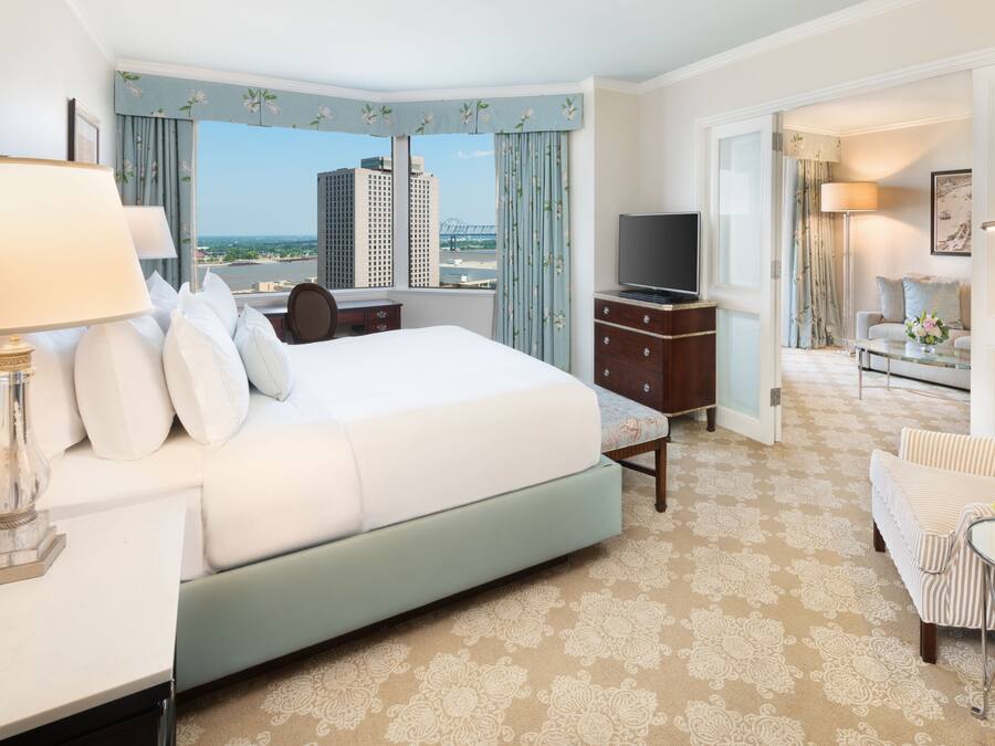 Quarto de hotel com uma cama grande, televisão, escrivaninha com luminária, cadeira e vista para a cidade.