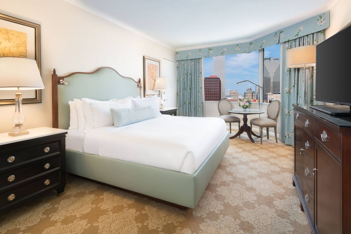 Quarto de hotel com cama, escrivaninha, poltrona, televisão e vista para a cidade.