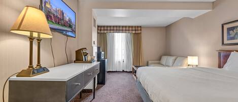 A hotel room with a bed, a desk with a lamp, a television, and a window with curtains.