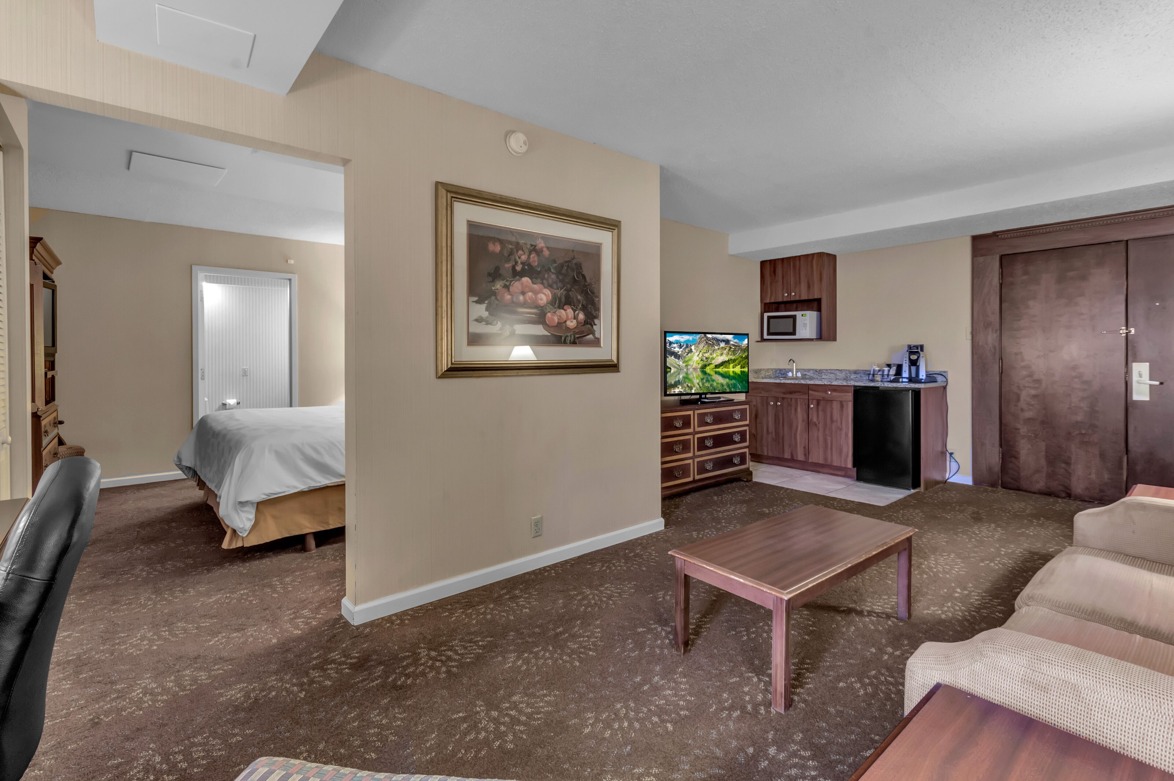 A hotel room with a bed, a desk, a sofa, a television, and a kitchenette.