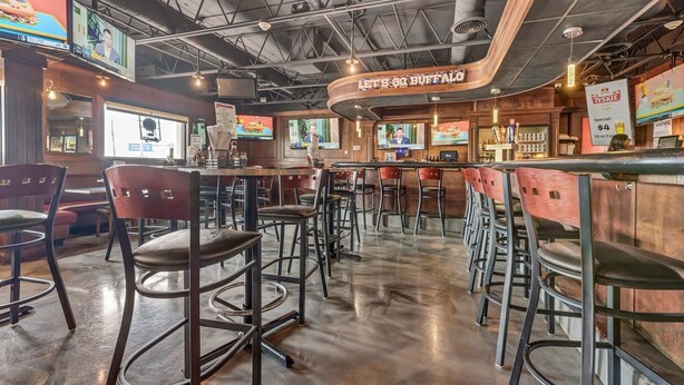A bar area with multiple stools, a counter, and TVs displaying sports.