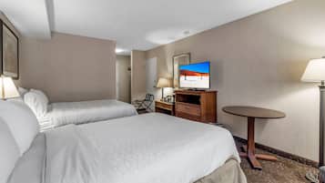 A hotel room with two beds, a desk, a chair, a TV, and a small table.