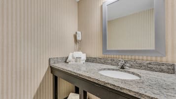 A bathroom with a granite countertop, a sink, a mirror, and a hairdryer on the wall.