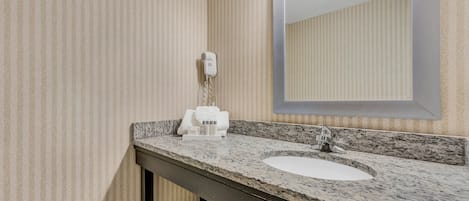 A bathroom with a granite countertop, a sink, a mirror, and a hairdryer on the wall.
