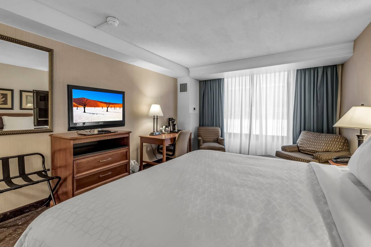 A hotel room with a large bed, a desk with a computer, a television, and a chair.