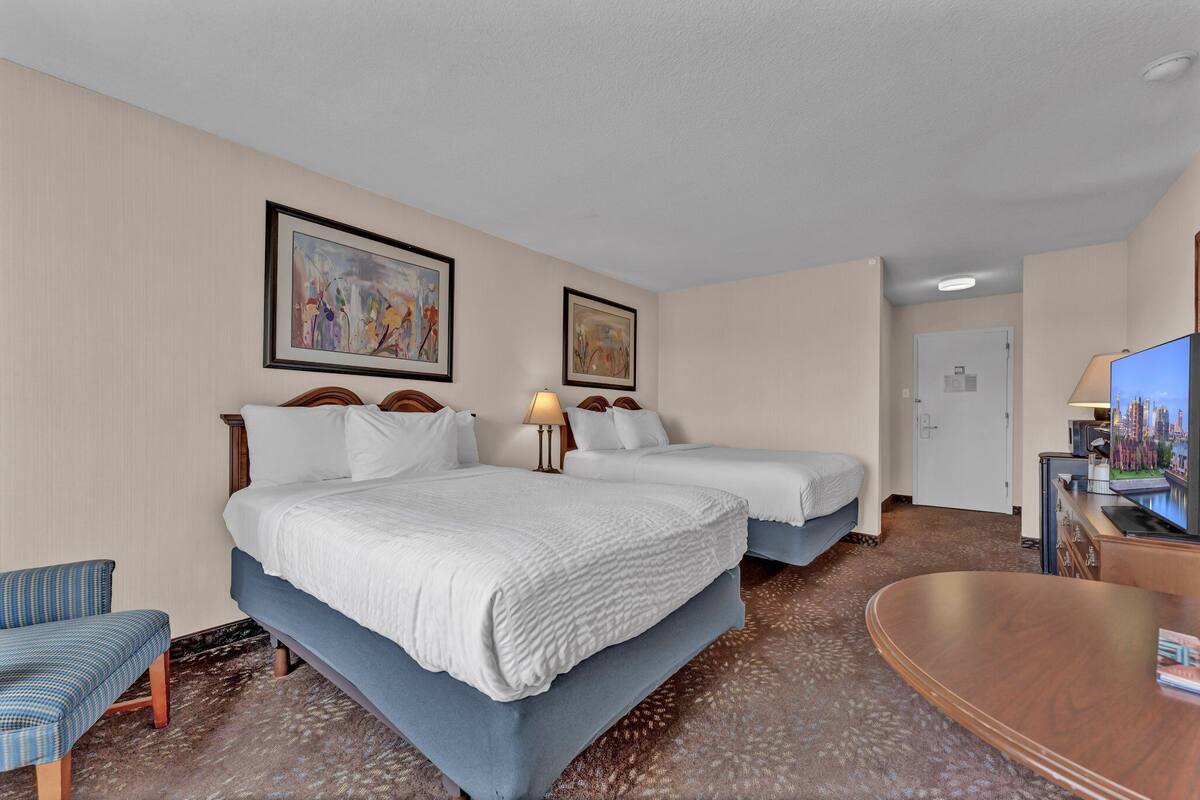 A hotel room with two beds, a desk with a TV, a chair, and artwork on the walls.