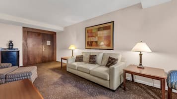 A hotel room with a beige sofa, two lamps, a coffee machine, and a framed abstract painting on the wall.