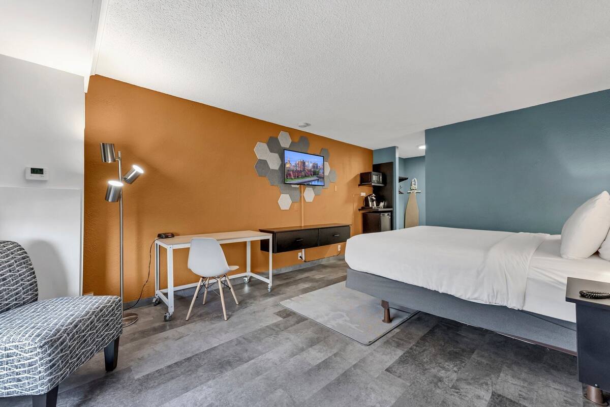 A modern hotel room with a bed, desk, chair, and a TV mounted on the wall.
