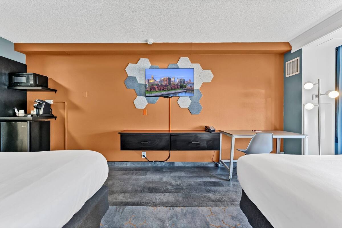 A hotel room with two beds, a desk, a chair, a TV mounted on the wall, and a microwave on the left.