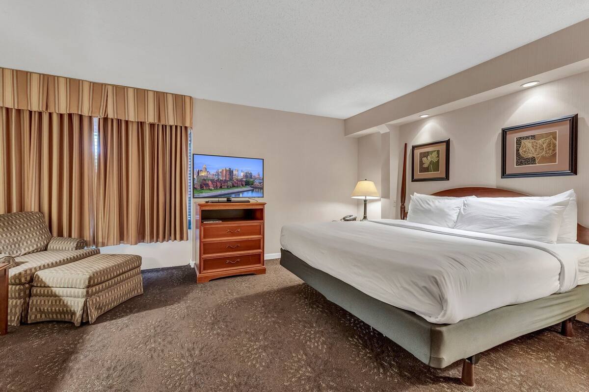 A hotel room with a bed, a TV, a desk, a chair, and a lamp.