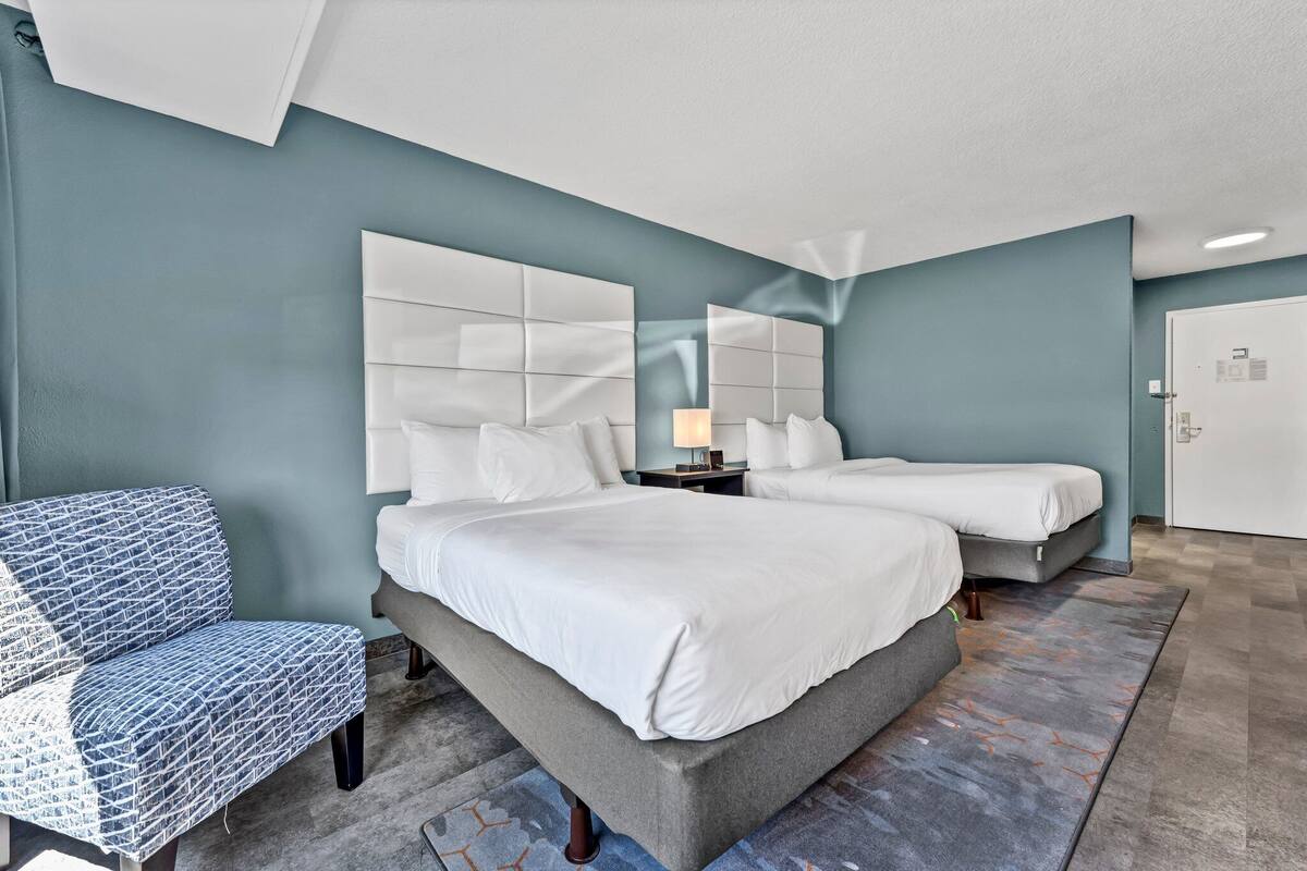 A modern hotel room with a large bed, two bedside tables, a chair, and a door.