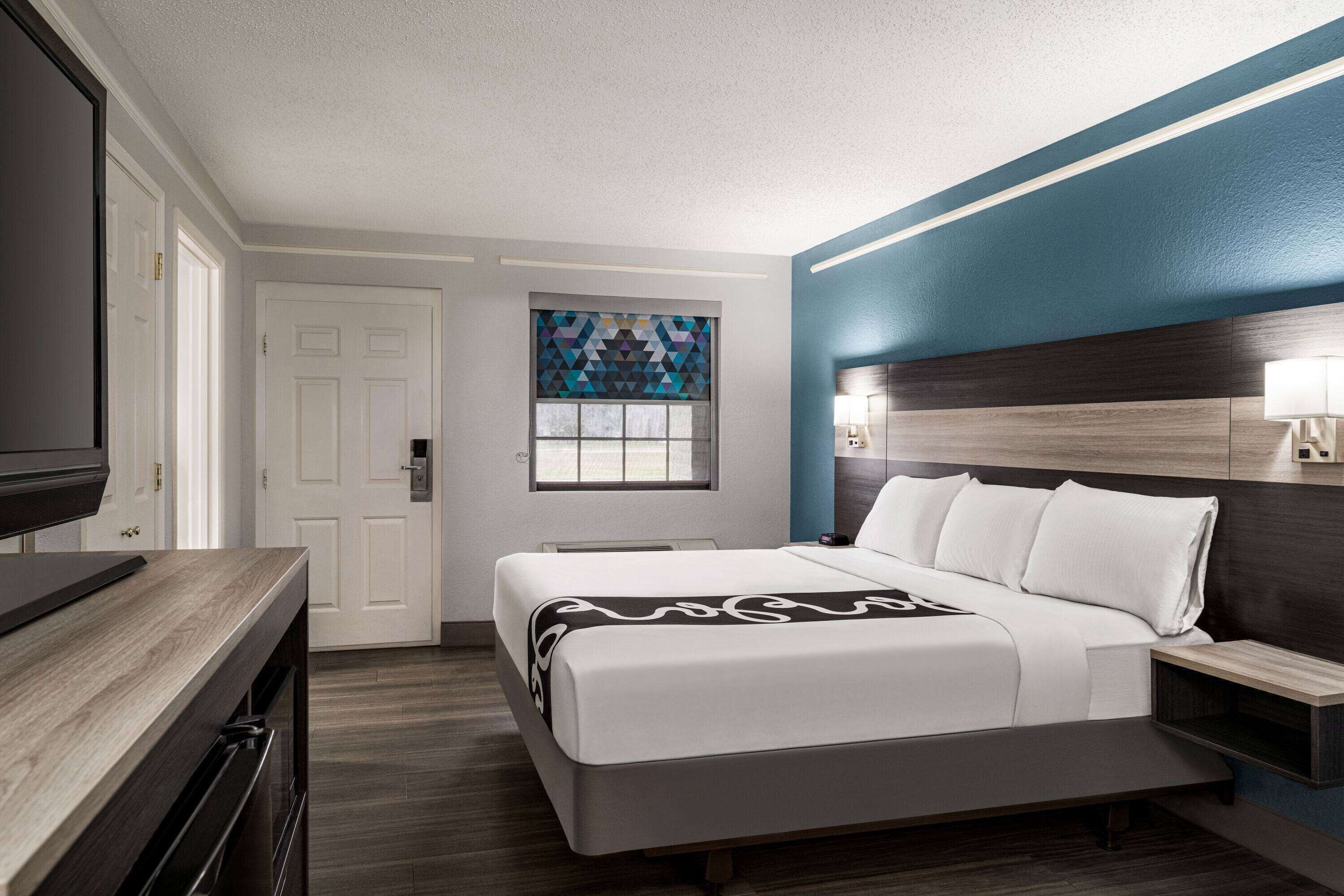 A modern hotel room with a large bed, a desk, and a TV.