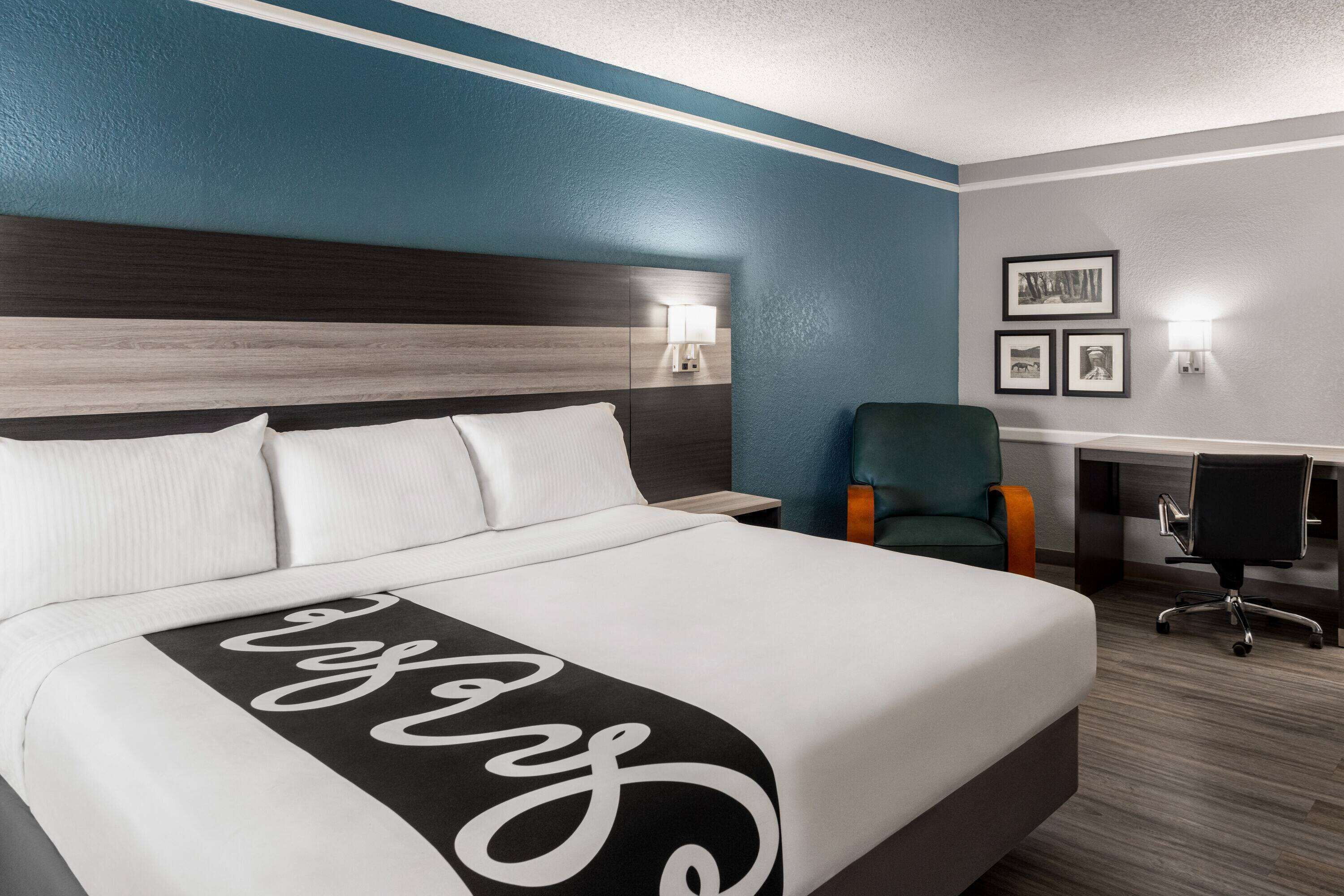 A hotel room with a large bed, a desk with a chair, and two wall-mounted lamps.