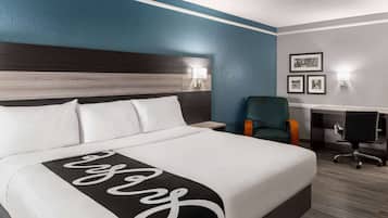 Una habitación de hotel con una cama grande, un escritorio con una silla y dos lámparas fijadas a la pared.