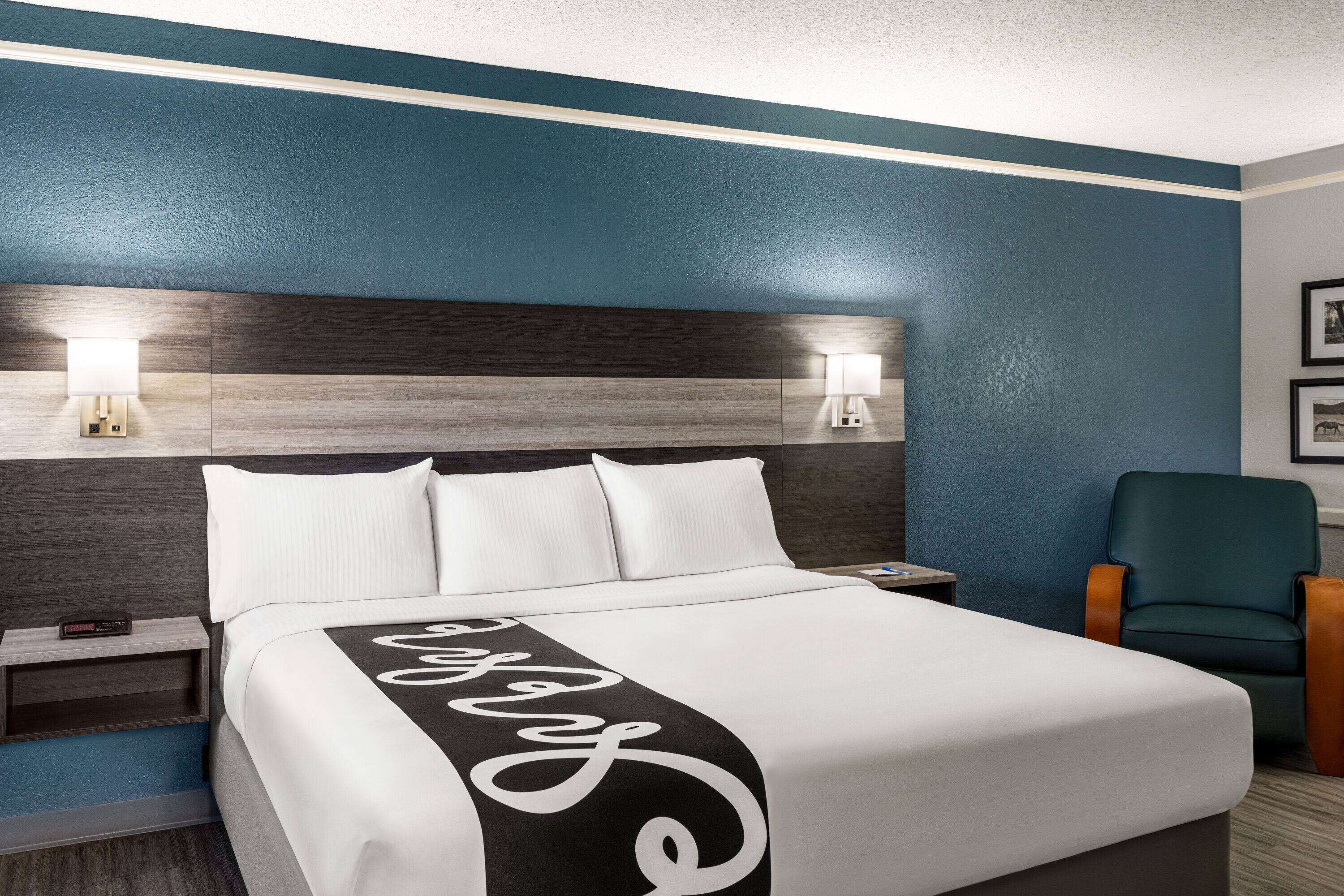 A hotel room with a large bed, two bedside tables with lamps, a chair, and a wall-mounted picture.