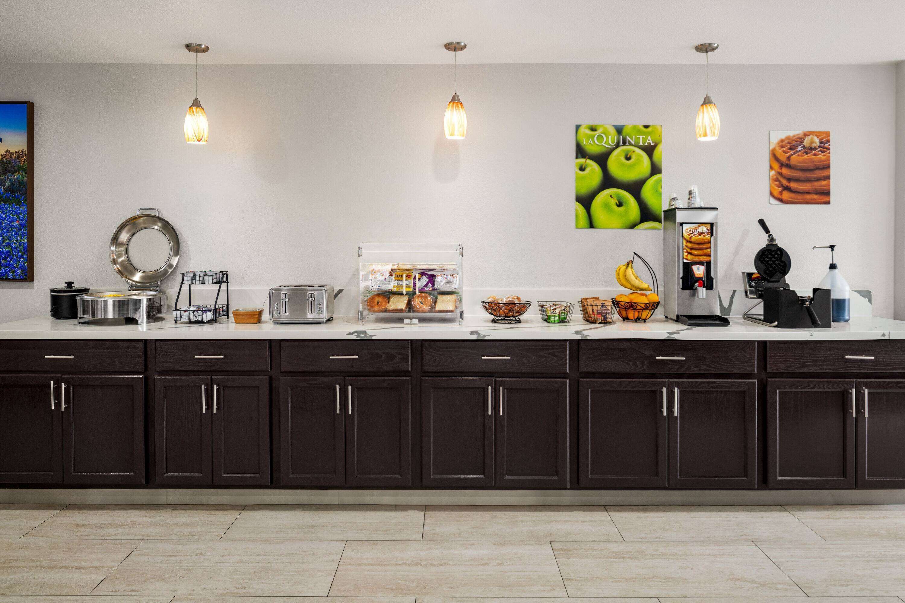 Una cocina moderna con armarios oscuros, una encimera con diversos electrodomésticos y alimentos, y decoración en la pared.