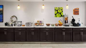 A modern kitchen with dark cabinets, a countertop with various appliances and food items, and decorative wall art.