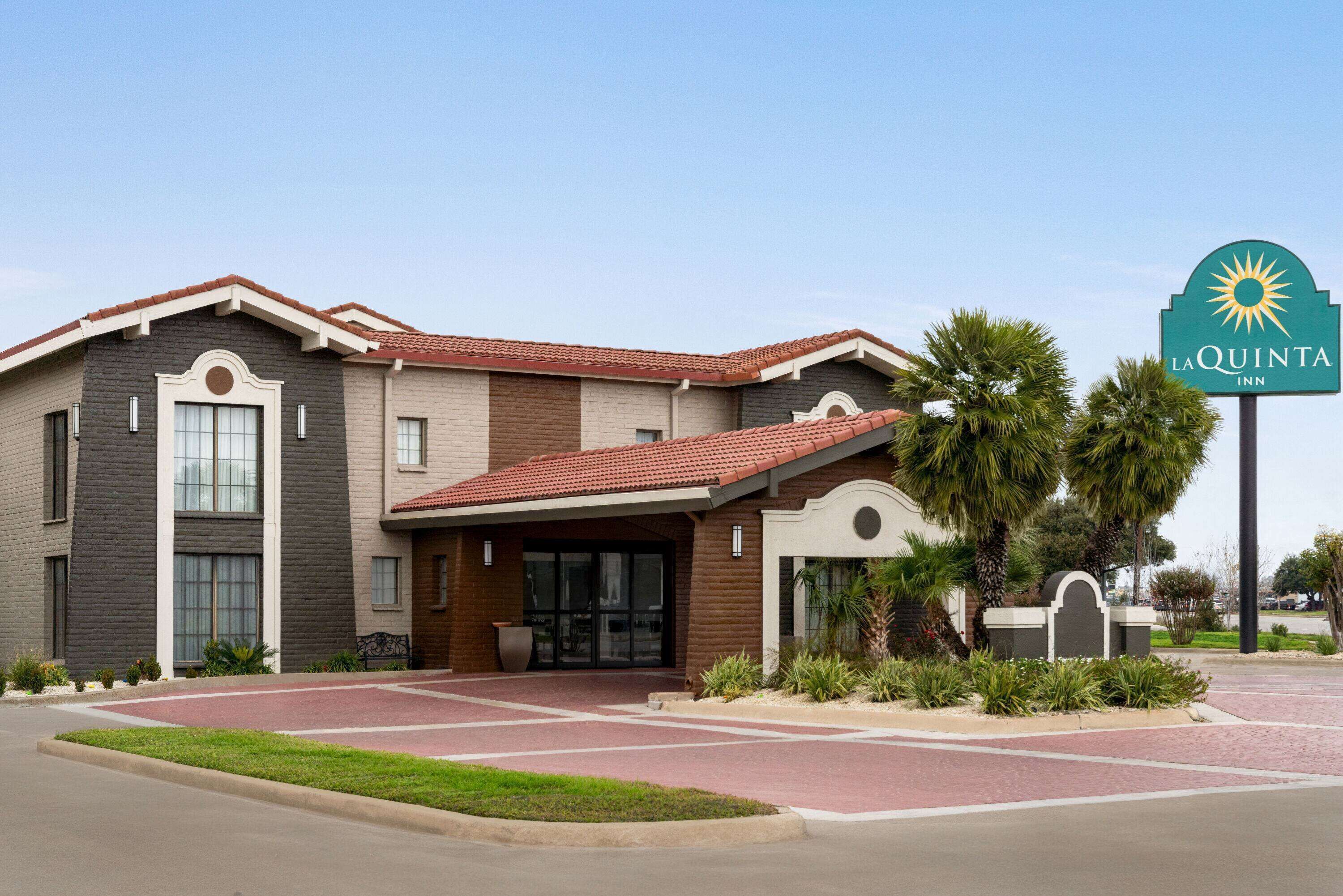 A La Quinta Inn hotel with a modern design, featuring a red-tiled roof, large windows, and a landscaped entrance area.