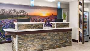 A reception desk with a stone facade, two computer monitors, and a mural of a sunset field. - La Quinta Inn by Wyndham Victoria (Victoria)