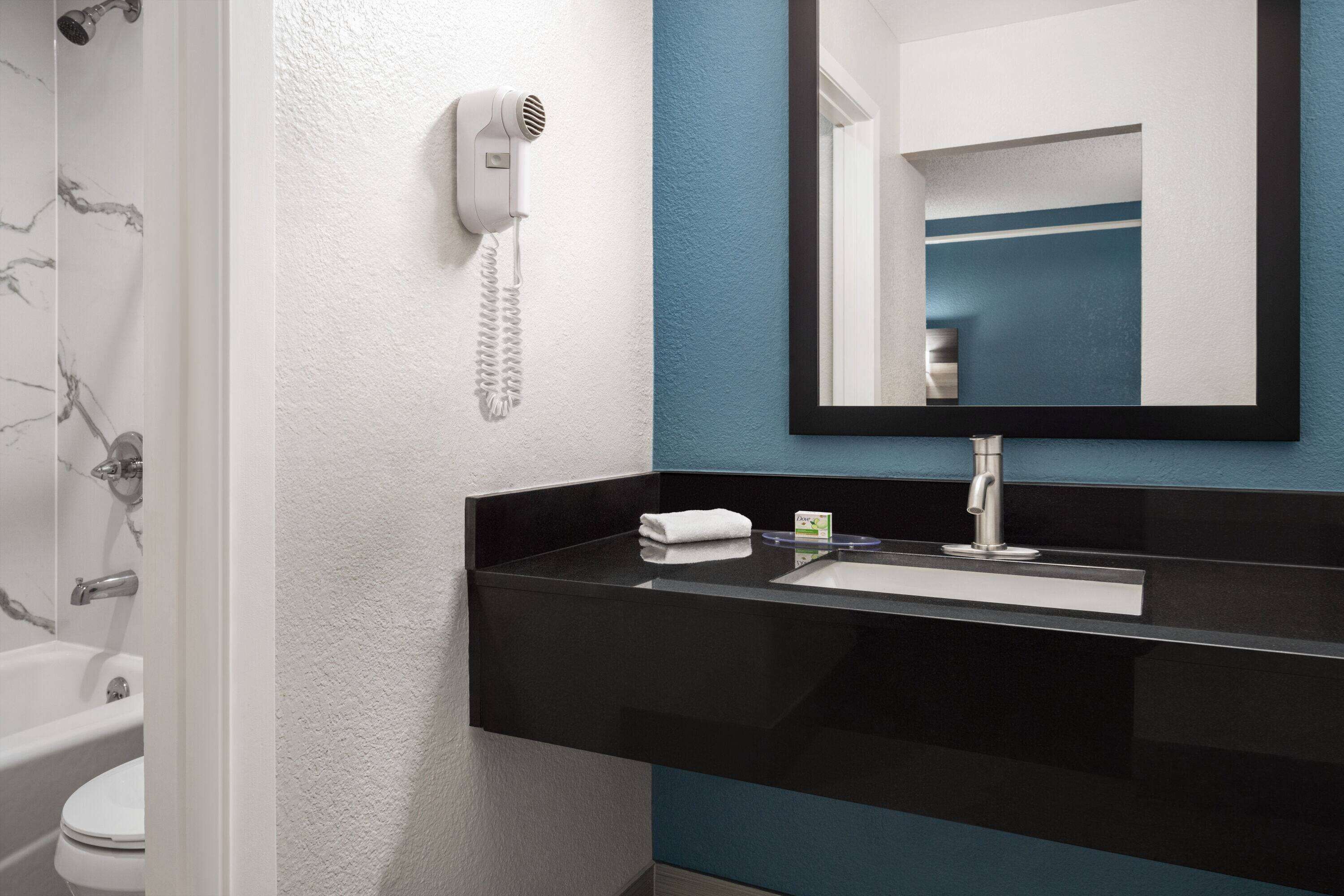 A modern bathroom with a black sink, a mirror, and a hairdryer mounted on the wall.