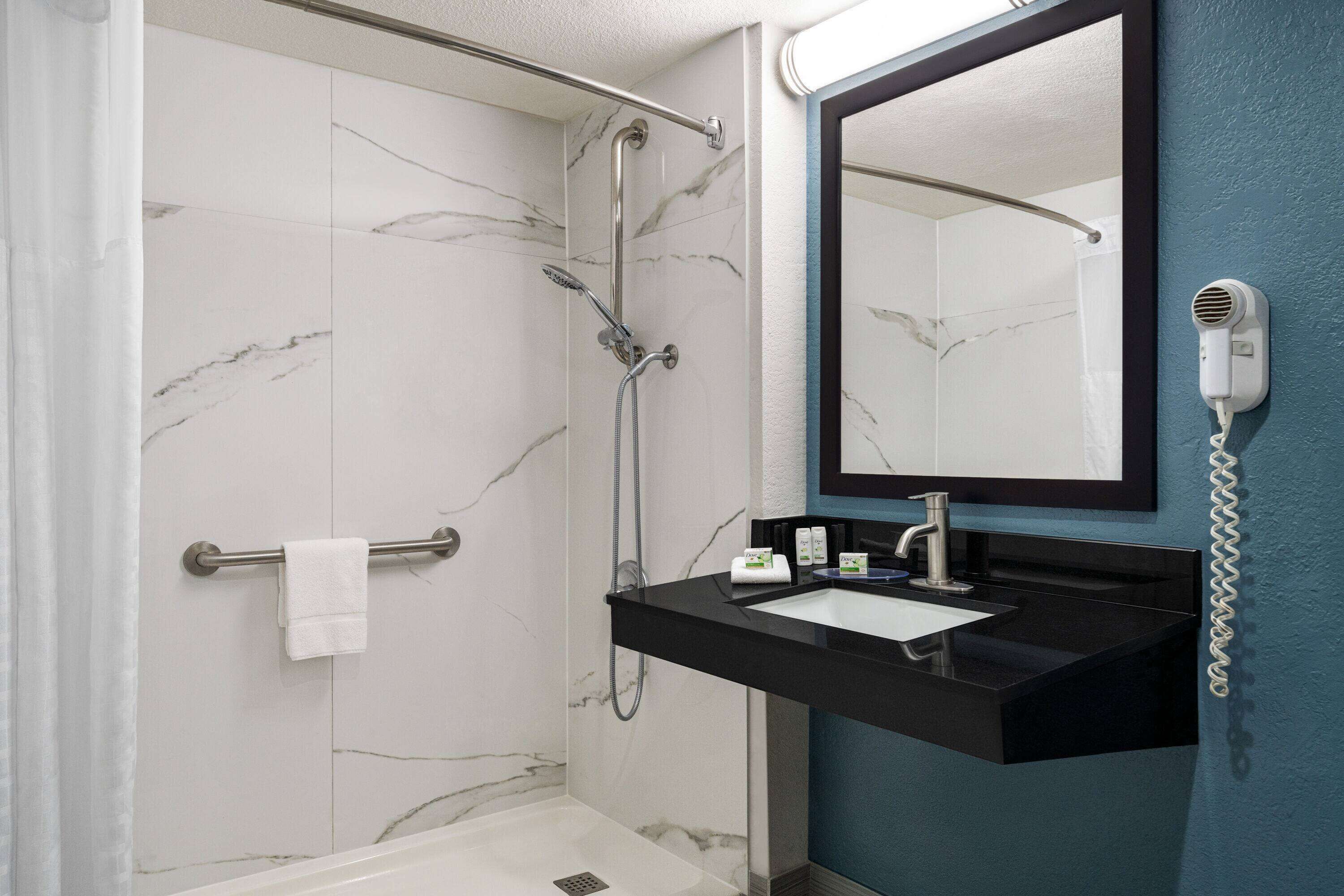 Een badkamer met een douche van marmer, een zwart wastafelmeubel, een spiegel en een haardroger bevestigd aan de muur.
