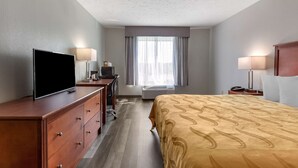 Habitación de hotel con cama, televisión, escritorio, lámpara y ventana con cortinas.