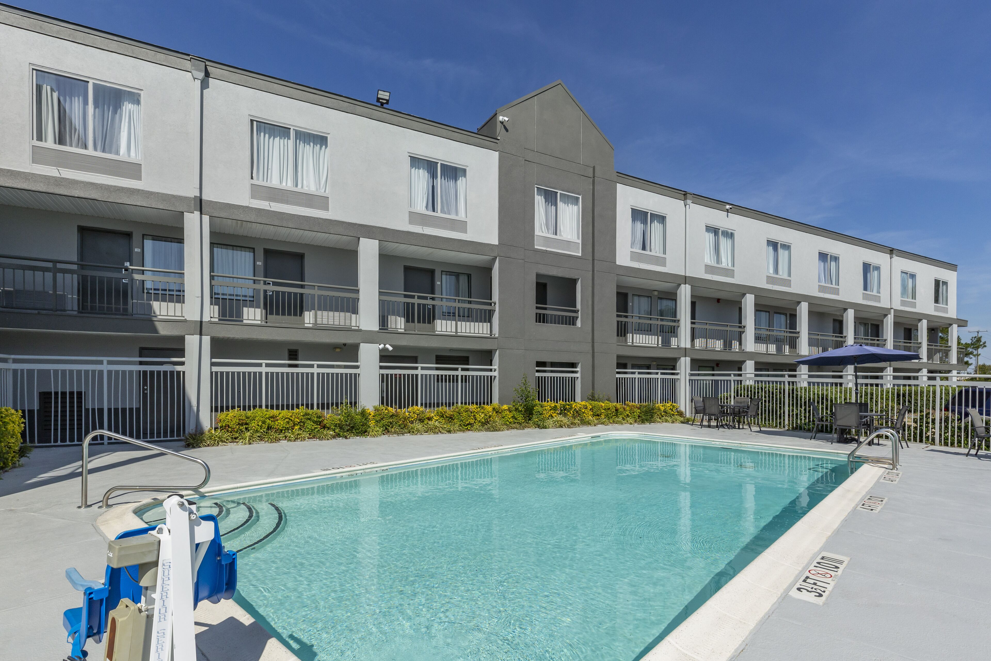 Un hotel moderno con piscina, diversi balconi e un cielo azzurro.