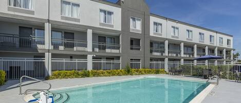 A modern hotel with a swimming pool, multiple balconies, and a clear blue sky.