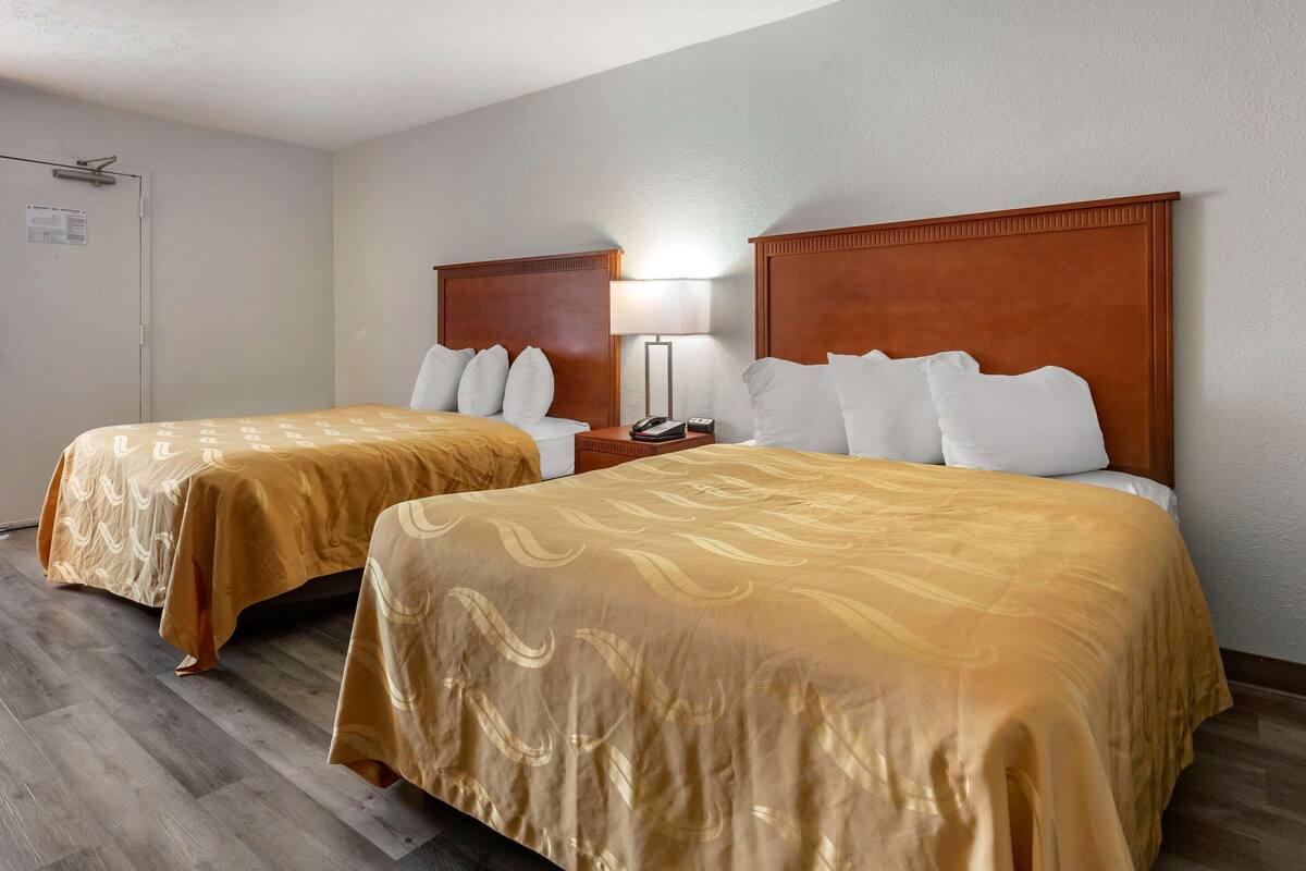 A hotel room with two beds, a nightstand with a lamp, and a door with a sign.