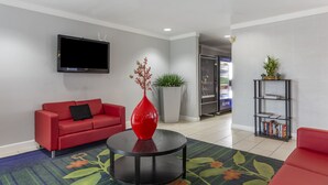 Un moderno vestíbulo de hotel con un sofá rojo, una mesa de centro negra con un jarrón rojo, una estantería y un televisor de pantalla plana montado en la pared.