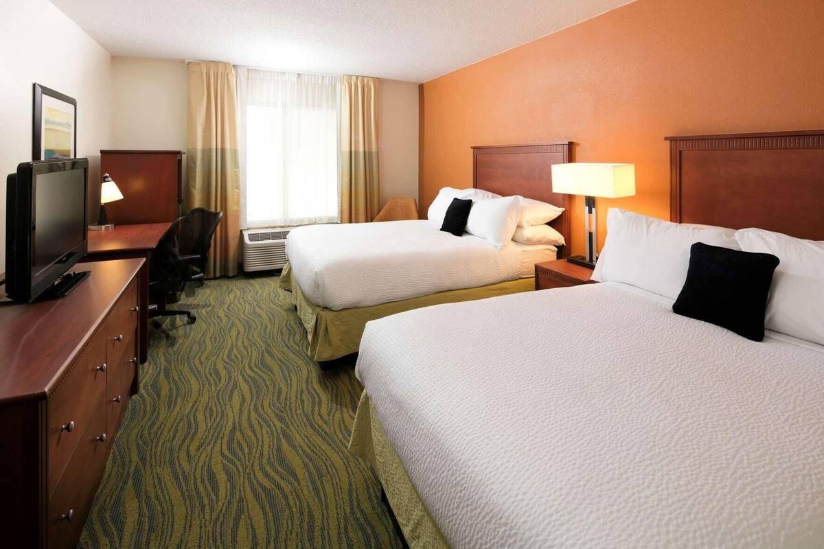 A hotel room with two beds, a desk with a television, a chair, and a window with curtains.