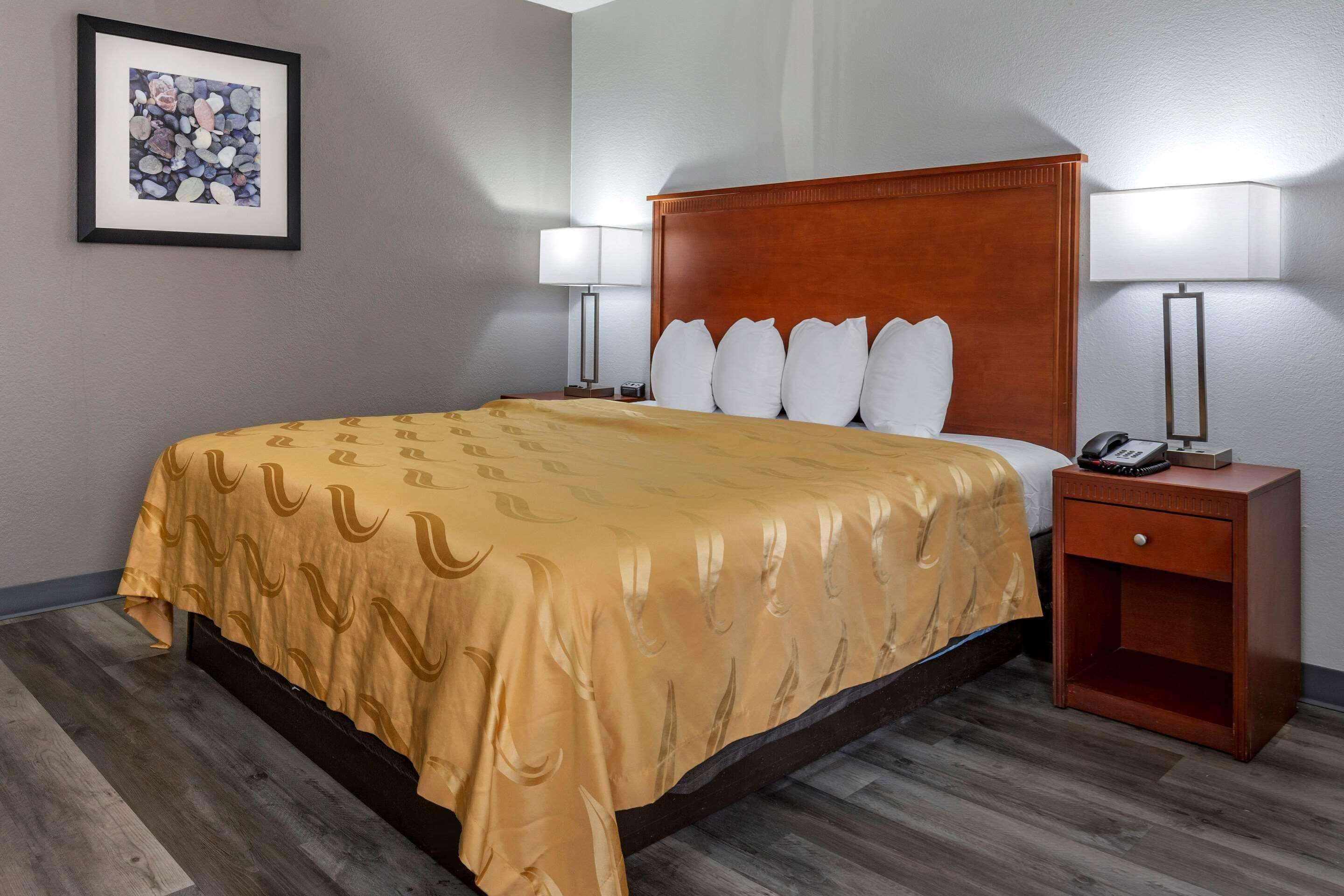 A hotel room with a bed, two bedside lamps, a nightstand with a phone, and a framed picture on the wall.