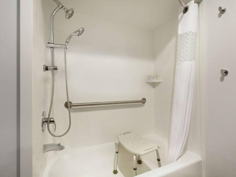 A bathroom with a shower, grab bar, and a wheelchair-accessible bench.